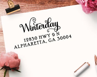May include: A white rectangular paper featuring black ink text that reads Winterday, 12850 HWY 9 N, ALPHARETTA, GA 30004. The word Winterday is in a decorative script font, while the address is in a clean, bold, sans-serif typeface.