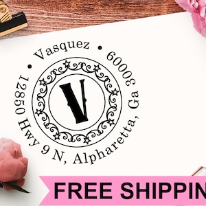 Puede incluir: Un sello de dirección de devolución redondo en blanco y negro con un borde decorativo y la letra "V" en el centro. El texto alrededor del borde dice "Vasquez, 12850 Hwy 9 N, Alpharetta, Ga 30006".