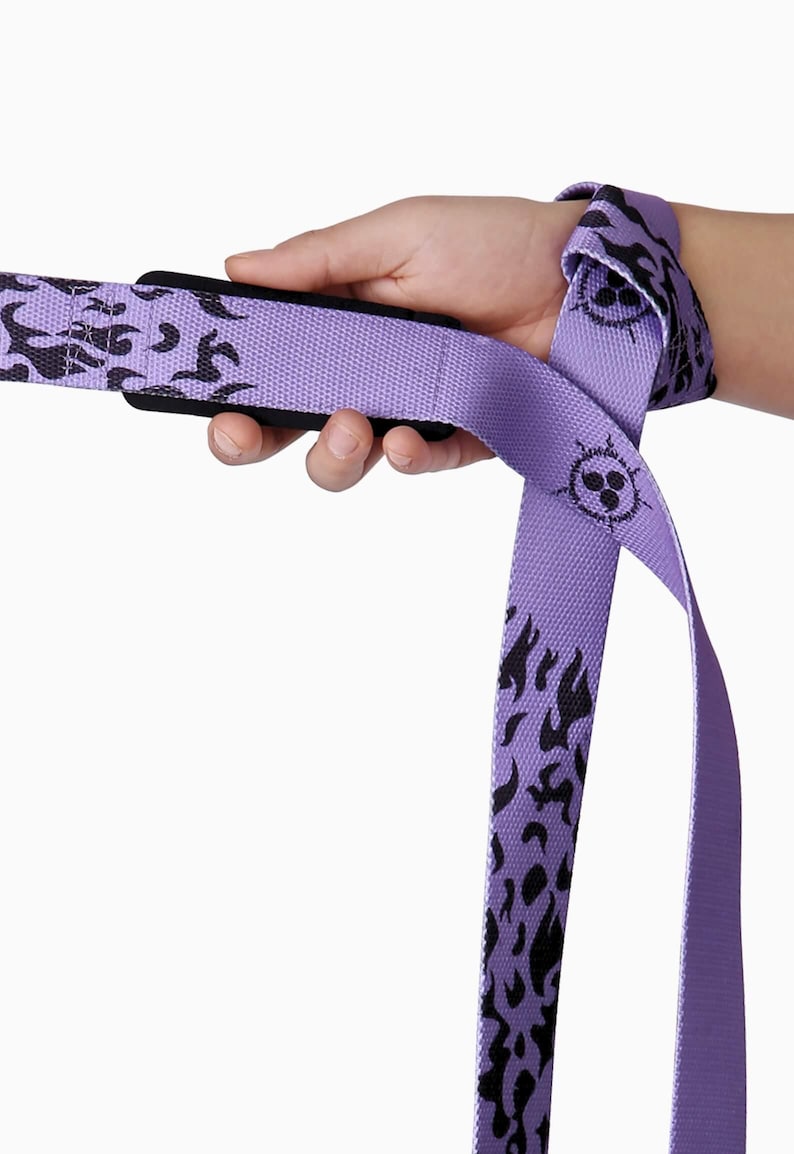 Purple anime lifting straps with black flame design being held. Heavy-duty powerlifting gear with character badge detail and secure loop construction for deadlifts and strength training.