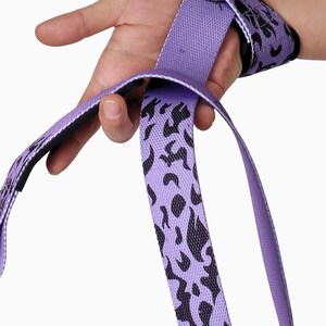 Purple anime lifting straps being wrapped around wrist showing flame pattern. Weightlifting wraps with secure loop closure for crossfit and strength training exercises.
