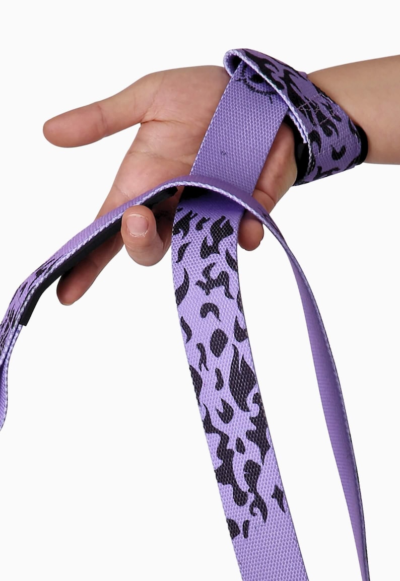 Purple anime lifting straps being wrapped around wrist showing flame pattern. Weightlifting wraps with secure loop closure for crossfit and strength training exercises.