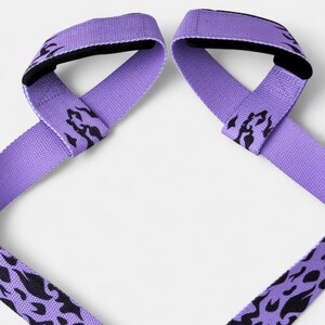 Pair of purple anime lifting straps with black flame patterns laid flat. Weight training gear featuring loop design for improved grip during deadlifts and heavy lifts.