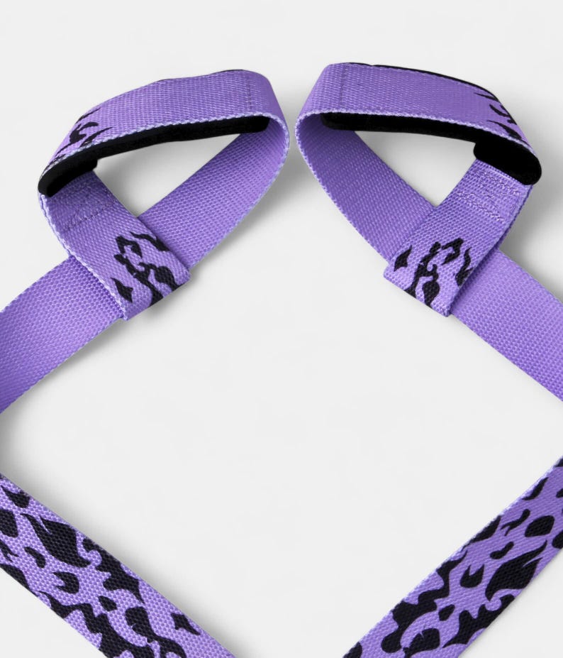 Pair of purple anime lifting straps with black flame patterns laid flat. Weight training gear featuring loop design for improved grip during deadlifts and heavy lifts.