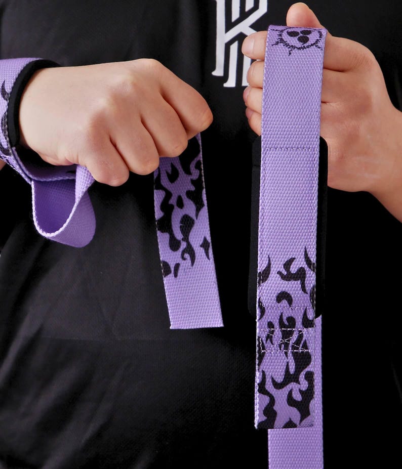 Hand demonstrating grip technique with purple anime wrist wraps featuring flame design. Deadlift straps with character badge showing proper wrapping for powerlifting.