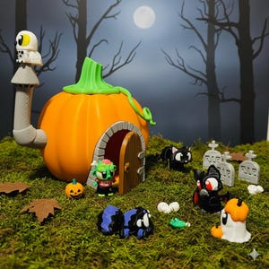Op de afbeelding: Een Halloween-diorama met een oranje pompoenhuis, groene stengel en schoorsteen met schedel. Miniatuurfiguren zijn onder meer een zombie, zwarte katten, een vleermuis en grafstenen, alles op groen mos.