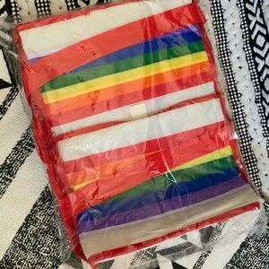 May include: A rainbow-colored tote bag with red handles. The bag is folded and packaged in plastic.