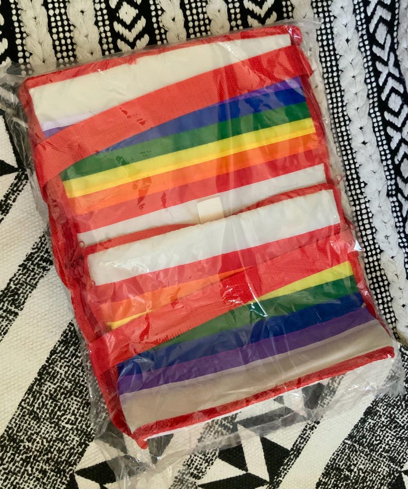 May include: A rainbow-colored tote bag with red handles. The bag is folded and packaged in plastic.