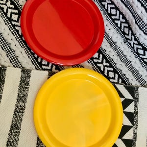 May include: Two round, plastic plates, one red and one yellow, on a black and white patterned surface.