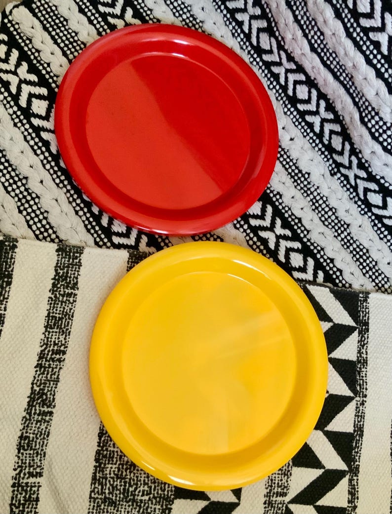 May include: Two round, plastic plates, one red and one yellow, on a black and white patterned surface.