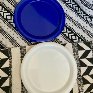 May include: Two round ceramic plates, one blue and one white, on a black and white patterned surface.