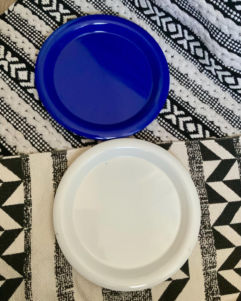 May include: Two round ceramic plates, one blue and one white, on a black and white patterned surface.
