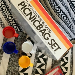 May include: A 21-piece insulated picnic bag set with a red, orange, and yellow striped box. The box has the text "21 PIECE NYLON/INSULATED PICNICBAG SET" and "1986 METRO MARKETING GARDENA, CA 90247 PO BOX 47170 ITEM #31-1842-00 MADE IN HONG KONG/CHINA".