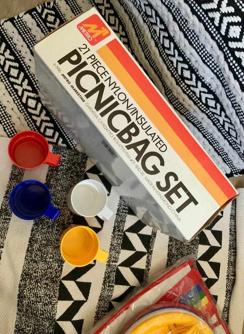 May include: A 21-piece insulated picnic bag set with a red, orange, and yellow striped box. The box has the text "21 PIECE NYLON/INSULATED PICNICBAG SET" and "1986 METRO MARKETING GARDENA, CA 90247 PO BOX 47170 ITEM #31-1842-00 MADE IN HONG KONG/CHINA".