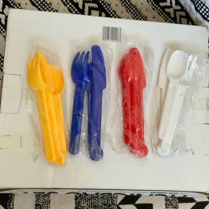 May include: A set of six plastic utensils in individual packaging. The utensils are yellow, blue, red, and white. The utensils include a fork, knife, and spoon.