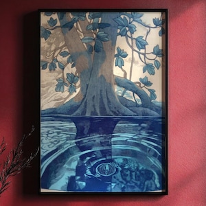 Könnte beinhalten: Gerahmtes Kunstwerk mit einem stilisierten Baum, der sich im Wasser spiegelt. Der Baumstamm und die Äste sind blau, mit blauen Blättern. Die Wasseroberfläche zeigt konzentrische Kreise. Das Kunstwerk ist in einem schwarzen Rahmen gerahmt.