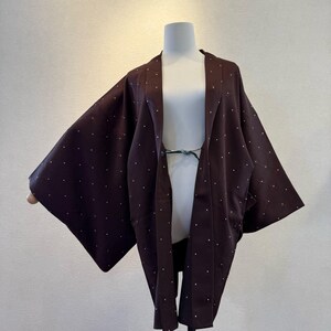 Puede incluir: Chaqueta marrón oscuro estilo kimono con lunares blancos. La chaqueta tiene mangas anchas y un corte holgado. La prenda se exhibe en un maniquí. La chaqueta está abierta por delante y tiene un cierre de lazo en la cintura.
