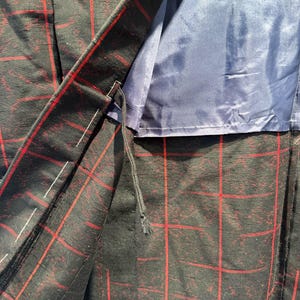 May include: Close-up of a black blazer with a red plaid pattern. The blazer's interior is lined with a solid blue fabric. The stitching and construction details are visible, showcasing the garment's tailoring.