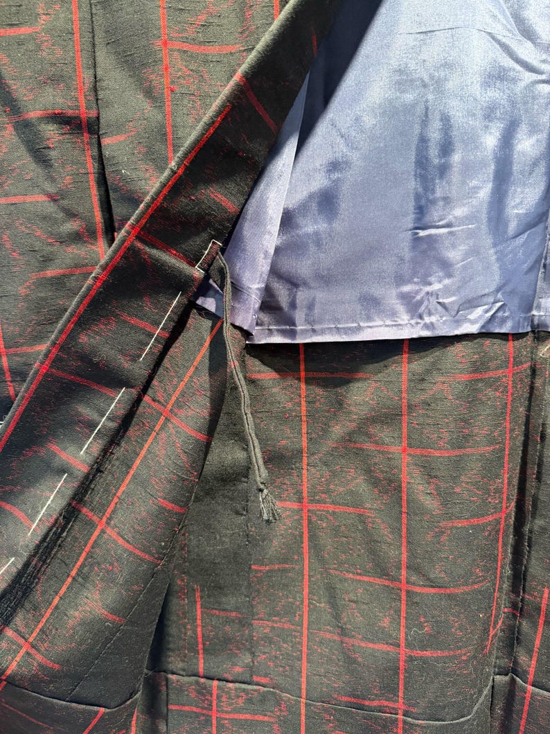 May include: Close-up of a black blazer with a red plaid pattern. The blazer's interior is lined with a solid blue fabric. The stitching and construction details are visible, showcasing the garment's tailoring.