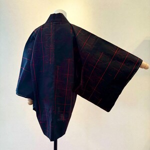 May include: A black kimono with a red plaid pattern, displayed on a mannequin. The kimono has wide sleeves and a collar. The fabric appears to be lightweight. The garment is displayed against a plain white background.