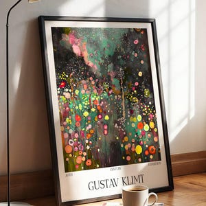 Op de afbeelding: Een ingelijste kunstdruk met een kleurrijk abstract bloemmotief van Gustav Klimt. Het kunstwerk toont een levendige mix van roze, gele, rode en groene tinten. Een kop koffie en een boek liggen op de houten vloer voor het kunstwerk.