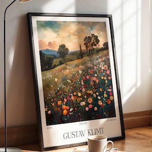 Op de afbeelding: Een ingelijste kunstdruk met een kleurrijk bloemenveld onder een bewolkte hemel. De print is gesigneerd "Gustav Klimt" en wordt tentoongesteld op een houten vloer naast een koffiekopje en een boek.