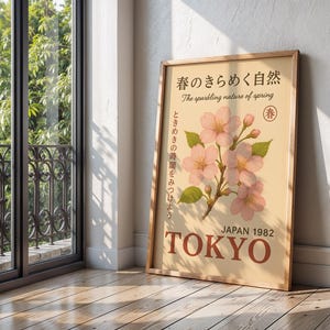 K&ouml;nnte beinhalten: Ein gerahmtes Poster mit hellbraunem Hintergrund zeigt rosa Kirschbl&uuml;ten und den Text "The sparkling nature of spring". Das Poster enth&auml;lt den Text "JAPAN 1982 TOKYO".