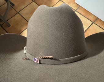 May include: A brown felt cowboy hat with a brown leather band and a small American flag pin.