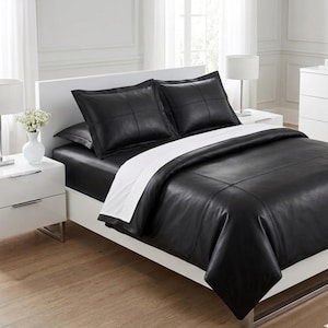 May include: A black leather-look bed set with a white accent. The set includes two square pillow shams, a fitted sheet, and a duvet cover. The pillows and duvet cover have a stitched, grid-like pattern. The bed is on a white frame.