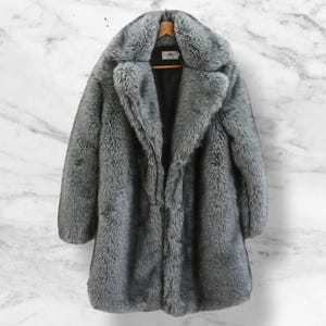 May include: A gray faux fur coat with a large collar. The coat is hanging on a wooden hanger.