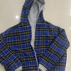 Può includere: Giacca con cappuccio a quadri blu con interno grigio e chiusura a zip completa. La giacca presenta un classico motivo a quadri blu, nero e giallo. Il cappuccio e i polsini sono di colore grigio.