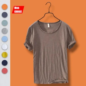Op de afbeelding: Een bruin T-shirt met ronde hals en opgerolde mouwen hangt aan een zwarte hanger tegen een oranje achtergrond. Het shirt heeft een eenvoudig, casual ontwerp. Een kleurenpalet van mogelijke shirtkleuren wordt links weergegeven, met de tekst "Men CHOICE" in een rode rechthoek.