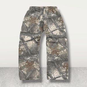 May include: Camouflage sweatpants in shades of brown, gray, and beige. The pants feature an elastic waistband and a relaxed fit. The Realtree Edge pattern is visible throughout the garment.