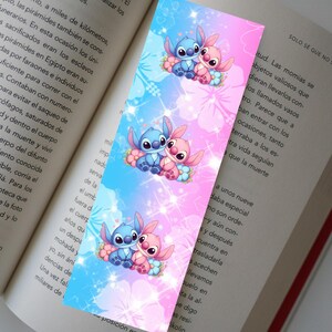 May include: A colorful bookmark featuring the characters Stitch and Angel from Lilo & Stitch. The design has a blue and pink gradient background with floral accents. The bookmark is rectangular and is placed on top of an open book.