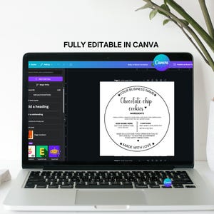 May include: A laptop displays a Canva design for a chocolate chip cookie label. The label is circular with text that reads "Your Business Name" and "Chocolate Chip Cookies." The ingredients and a "Made with Love" message are also included.