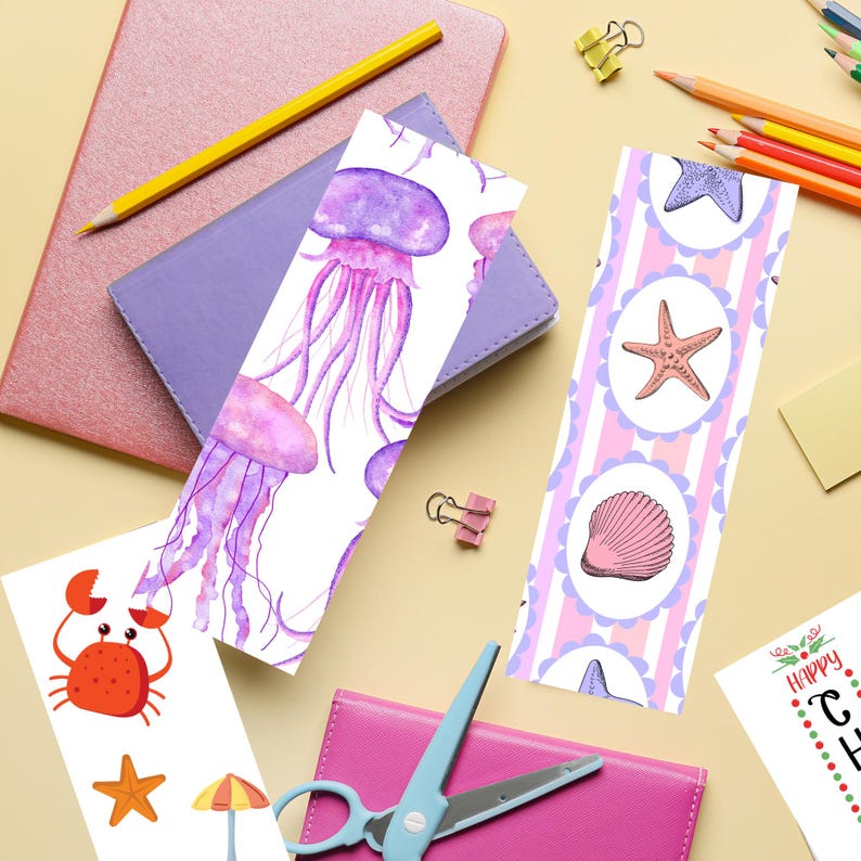 May include: A collection of colorful bookmarks with marine life illustrations, including jellyfish, starfish, and seashells. The bookmarks are placed near a purple notebook, a yellow pencil, and other stationery items. The overall theme is related to the ocean and summer.