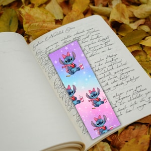 May include: A colorful bookmark featuring a cartoon character with a pink bow, scarf, and drink. The bookmark has a gradient background with stars and is placed on an open book with handwritten text.