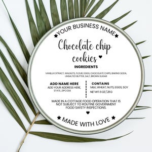 May include: A round tin with a label that reads "Chocolate chip cookies." The label lists ingredients and allergen information. The tin is surrounded by green palm leaves. The net weight is 6 oz / 211 g.