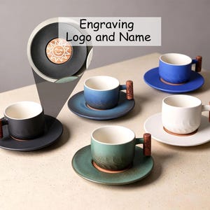 May include: Four ceramic cups and saucers in black, blue, white, and green with a gradient finish. Each cup features a cylindrical wooden handle with an engraved name. A circular inset shows a sun icon engraving. Text reads Engraving Logo and Name.