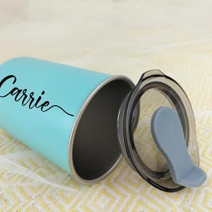 May include: A light blue tumbler with a black lid and a gray mouthpiece. The tumbler has the name "Carrie" in a black script font. The tumbler is made of stainless steel and is designed to keep drinks cold or hot.