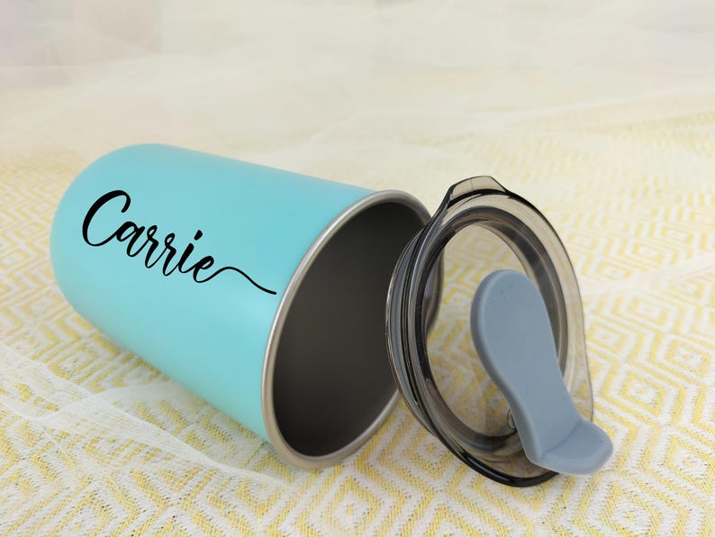 May include: A light blue tumbler with a black lid and a gray mouthpiece. The tumbler has the name "Carrie" in a black script font. The tumbler is made of stainless steel and is designed to keep drinks cold or hot.