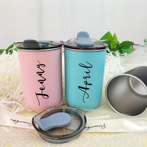 May include: Two insulated tumblers, one pink and one teal, with black lids and the names "Jenny" and "April" in script. A third black tumbler is visible, along with a lid. The tumblers are on a white surface.