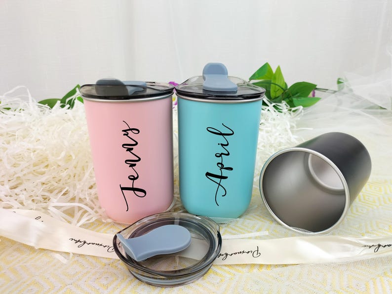 May include: Two insulated tumblers, one pink and one teal, with black lids and the names "Jenny" and "April" in script. A third black tumbler is visible, along with a lid. The tumblers are on a white surface.