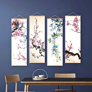 Puede incluir: Cuatro obras de arte murales verticales con diseños florales. Cada pieza presenta una rama diferente de flores rosas y rojas sobre un fondo blanco. El arte está enmarcado con varillas de madera y colgado con cuerda.