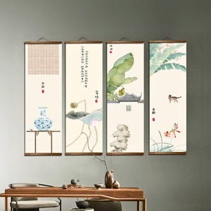 Pode incluir: Quatro painéis verticais de arte de parede com pinturas em aquarela de inspiração asiática. Os painéis apresentam um vaso, uma flor de lótus, um edifício com uma folha grande e um gato com flores. Cada painel tem varas de madeira na parte superior e inferior.