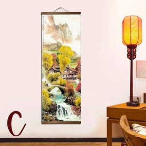 May include: A vertical wall scroll featuring a landscape painting with mountains, trees, and houses. The artwork uses warm colors, including yellow, red, and brown, to depict an autumn scene with a waterfall and a stone bridge.