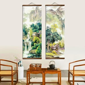 May include: Two vertical landscape paintings depicting waterfalls, mountains, and traditional Asian architecture. The artwork features a color palette of greens, blues, and browns, with wooden hanging rods at the top.