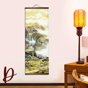 May include: A vertical landscape painting depicting a mountain scene with a waterfall, trees, and a small village. The artwork features a muted color palette of greens, yellows, and browns, with a wooden hanging rod at the top. The painting evokes a sense of tranquility.