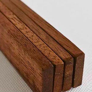 May include: Close-up of four rectangular wooden pieces. The wood has a rich, dark brown color with visible grain patterns. The pieces are stacked together, showcasing their uniform shape and size. The wood appears to be smooth and well-finished.