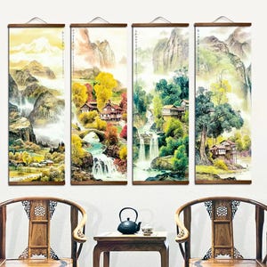 May include: Four vertical landscape paintings depicting waterfalls, mountains, and traditional houses. The artwork features a blend of yellow, green, and brown hues, with wooden hanging rods at the top. The paintings are displayed above a small table and two wooden chairs.