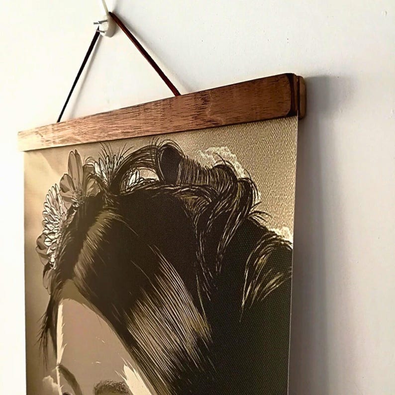 May include: A sepia-toned art print of a woman's face, adorned with a flower in her hair, is displayed on a wall. The print is held by a wooden frame and suspended by a brown cord, creating a vintage aesthetic.
